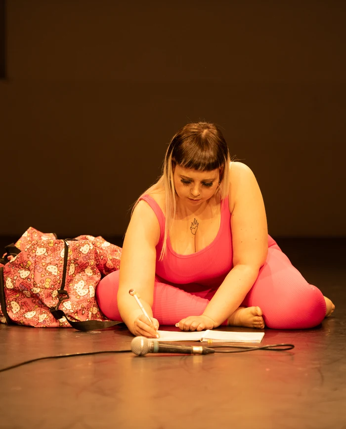 Un’artista vestita di rosa, seduta sul palco con un microfono