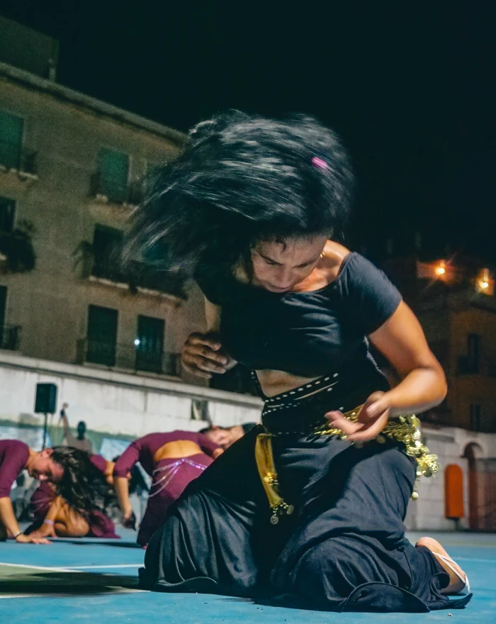 Una danzatrice in ginocchio durante una performance serale in piazza